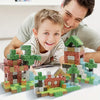 A young boy is smiling while building a miniature landscape using colorful magnetic building cubes.