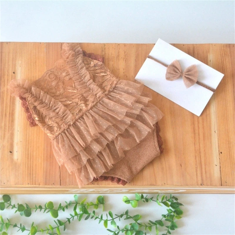 A brown lace baby romper with ruffled details and a matching brown bow headband displayed on a wooden board.