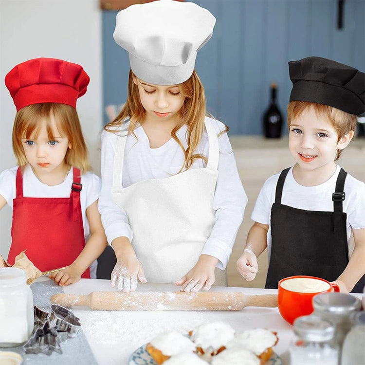 Two children wearing chef aprons and hats are preparing food on a kitchen counter.