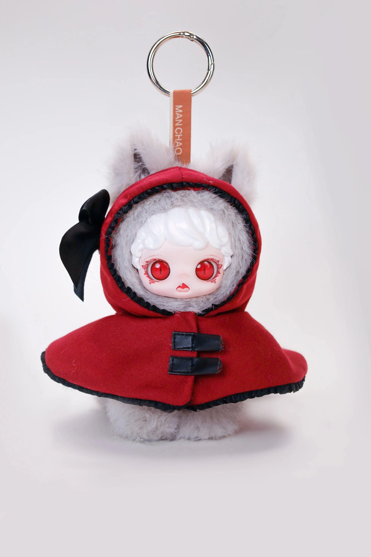 A red hooded plush doll with white hair and large red eyes, featuring a black bow and a metal keyring.
