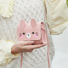 A pink mini PU leather crossbody handbag with a cute rabbit face design is held in a person's hand.