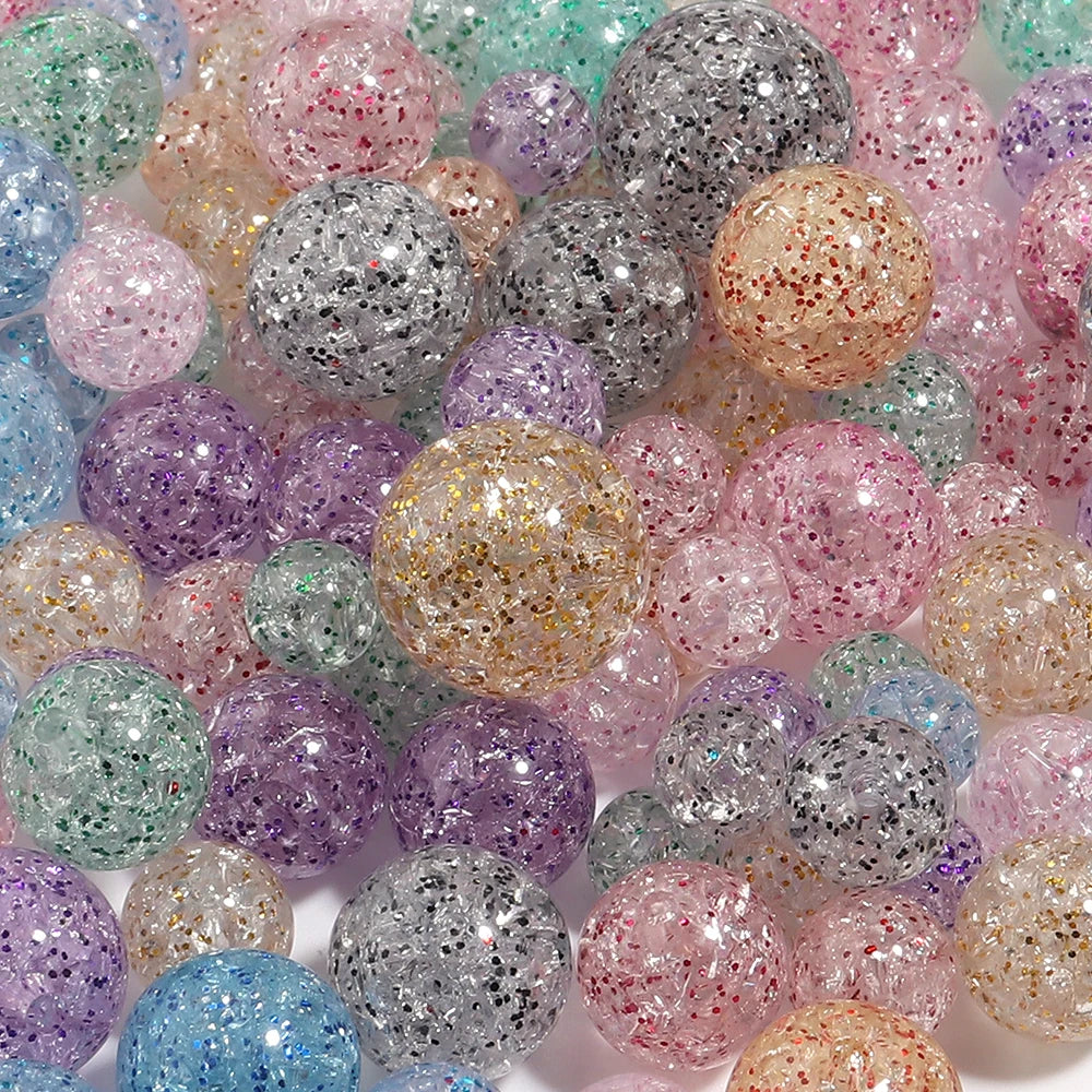 A close-up view of various round loose glitter cracked acrylic beads in shades of pink, purple, silver, and clear.