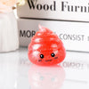 A bright red glitter squishy stress ball with a cute, smiling face resting on a reflective surface.