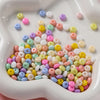 A close-up view of a white dish filled with various colored glass spacer beads including pink, yellow, blue, and white shades