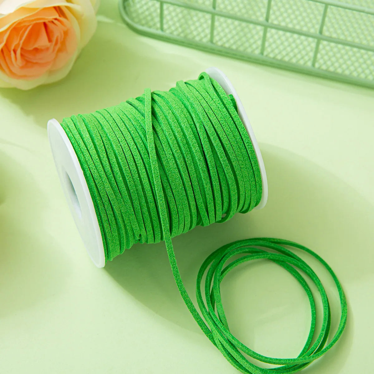 A roll of bright green velvet faux suede braided ribbon for crafting and gift wrapping is shown on a light green surface.