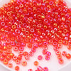A pile of small, translucent red and orange glass rice beads for DIY jewelry and crafting.