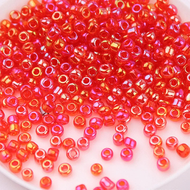 A pile of small, translucent red and orange glass rice beads for DIY jewelry and crafting.