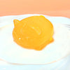 A bright yellow, squishy cat toy resting on a white plate.