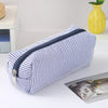 A striped blue and white canvas pencil case with a zipper is shown lying on a white surface.
