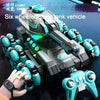 A black and teal six-wheeled stunt tank vehicle is shown with a hand holding a controller.