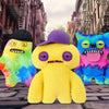 A yellow, fuzzy monster plush toy with purple accents sits in an outdoor setting.