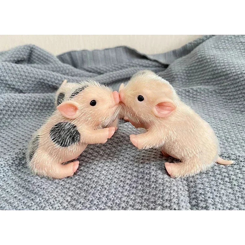 Two small, realistic soft silicone piglet mini dolls are positioned facing each other on a gray knitted fabric.