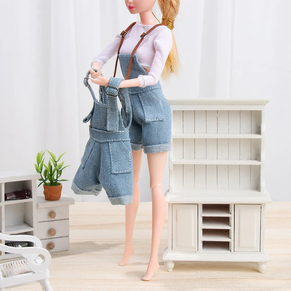 A mini doll wearing a denim overalls set and white t-shirt standing in front of a white wooden cabinet.