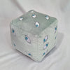 A soft, light gray plush figure shaped like a cube with various stylized eye designs.
