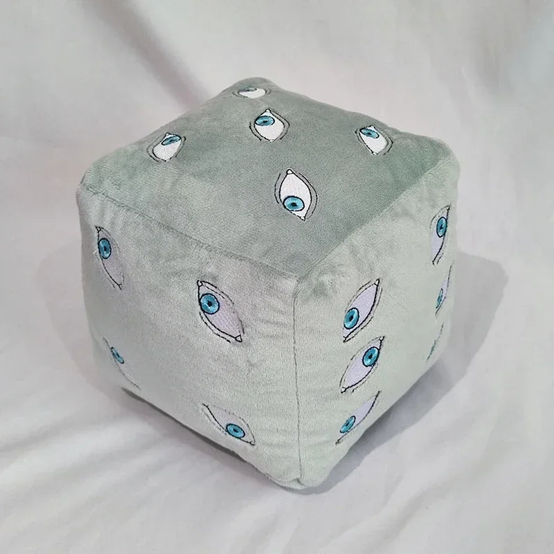 A soft, light gray plush figure shaped like a cube with various stylized eye designs.