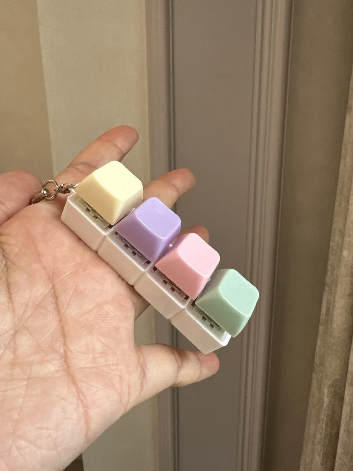 A hand holds a fidget keychain stress reliever with five colorful, square keys.