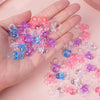 A hand holds a variety of mini acrylic pacifier party favors in shades of pink, purple, and blue.