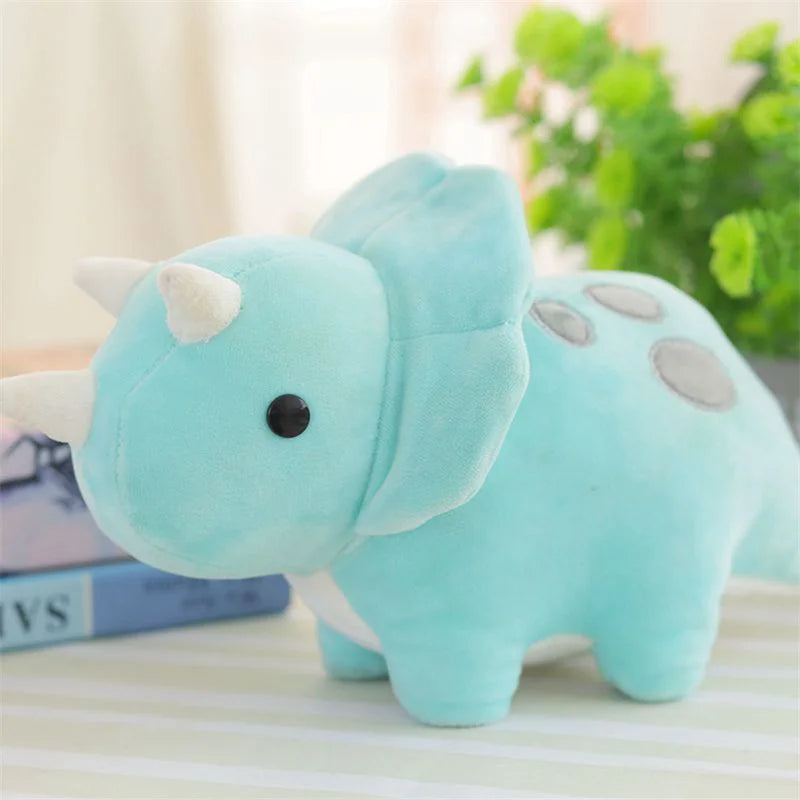 A light blue soft plush toy of a triceratops dinosaur resting on a white surface.
