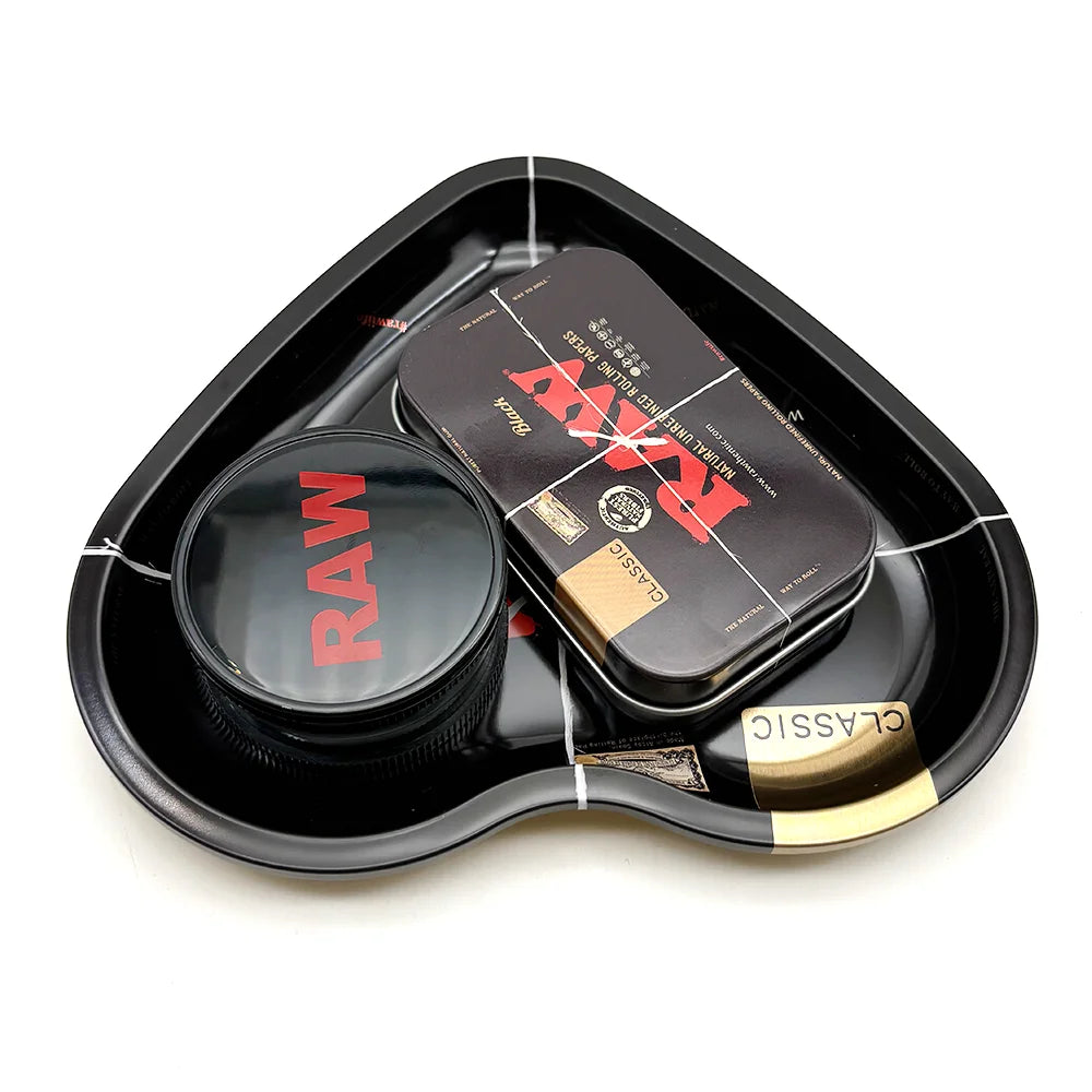 A black love-shaped metal rolling tray holds a glass jar and a rectangular metal herb grinder.