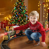 A smiling young boy plays with a musical Christmas train set featuring Santa and a snowman on a wooden track.