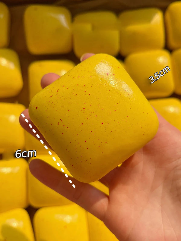 A hand holds a bright yellow squishy simulated bread fidget toy with a red speckled surface.