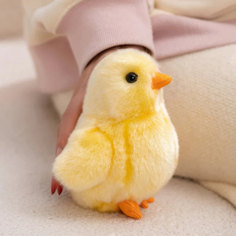A small, fluffy yellow chick plush toy with orange feet is held by a person's hand.