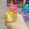 Une main tient un jouet anti-stress jaune et brillant à presser, à côté de plusieurs cubes en plastique colorés.
