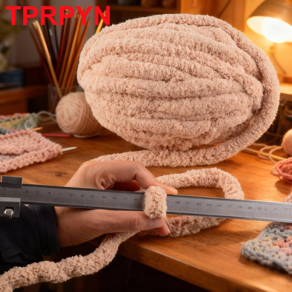 A hand measures a large ball of light pink chunky chenille yarn used for knitting or crafting.
