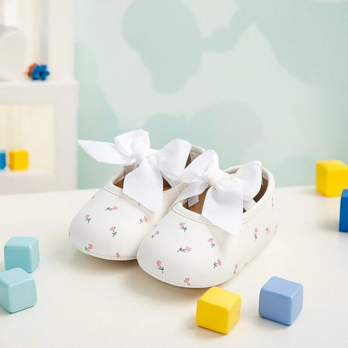 Ein Paar weiße, mit Blumenmuster bedruckte Sandalen für Säuglinge und Kleinkinder auf einer weißen Oberfläche mit bunten Bloc