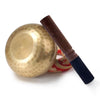 A golden Tibetan singing bowl with a dark wooden mallet and silk cushion.