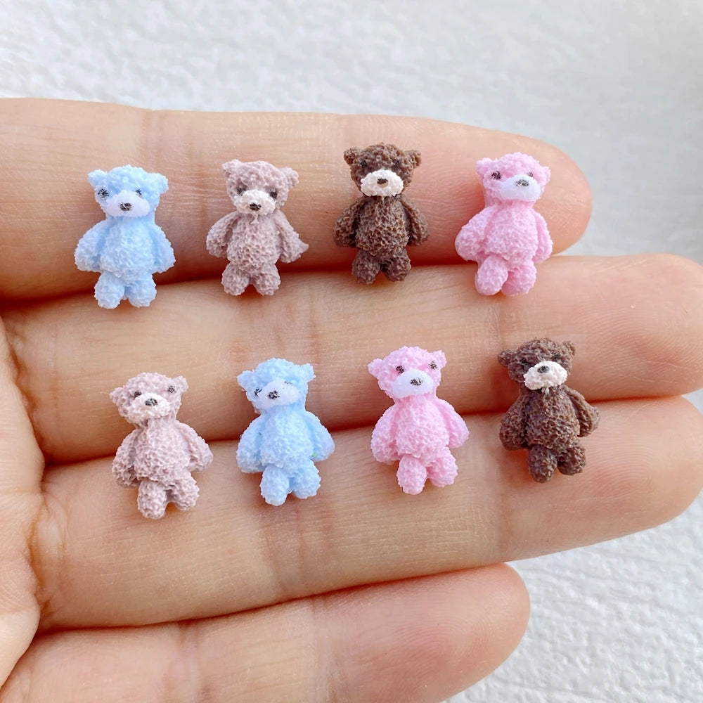 A hand holds several small resin teddy bear charms in various pastel colors including blue, pink, and brown.