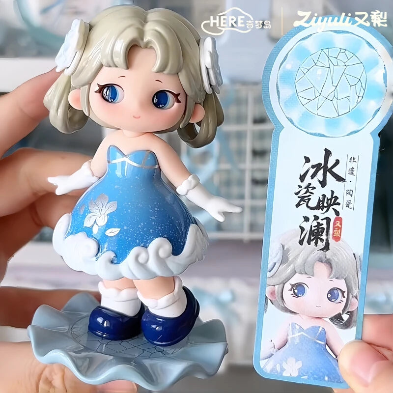 A collectible figurine of a girl with light hair and blue eyes wearing a blue dress and white accents, displayed on a clear s