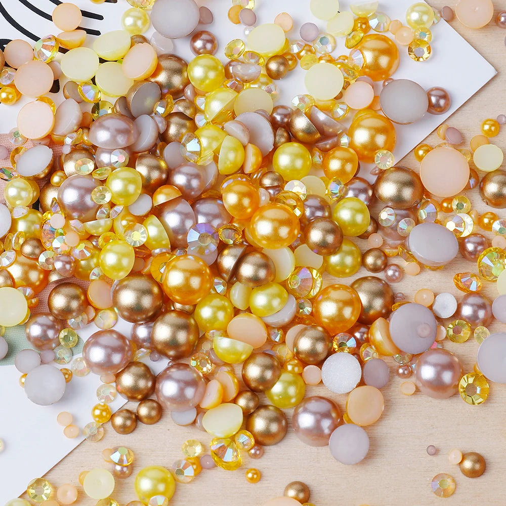 A close-up of mixed resin rhinestone pearls in shades of gold, amber, and lilac with an AB finish scattered on a light wooden
