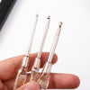 A hand holds a set of seven aluminum crochet hooks with color-coded handles against a white background.