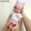 A newborn baby doll wearing a pink striped hat and diaper, held by a hand.