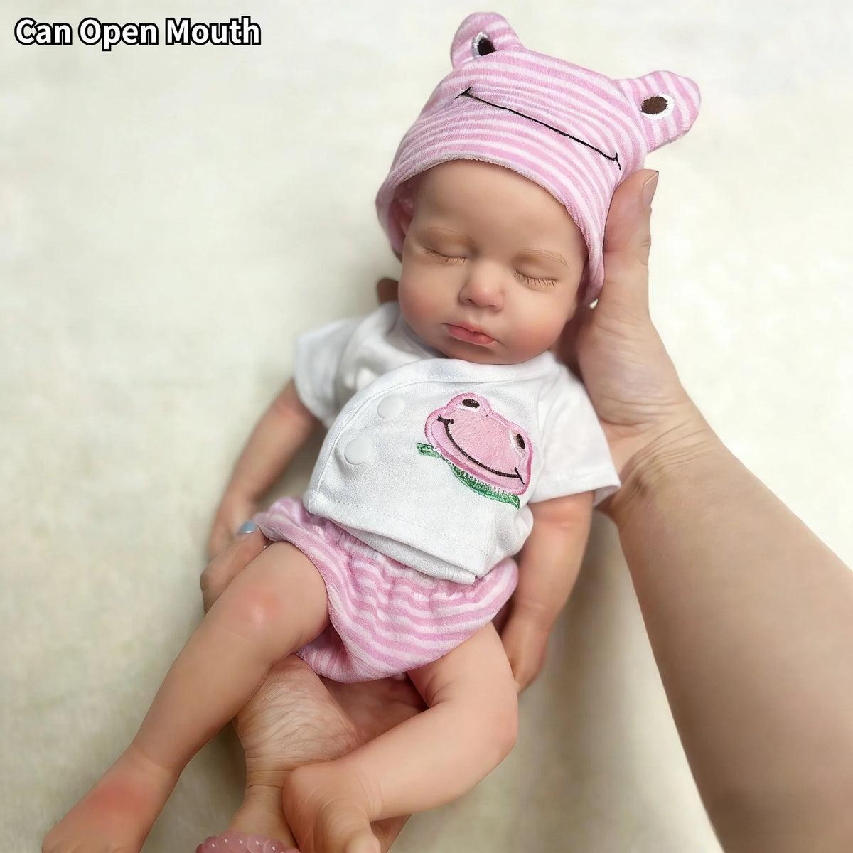 A newborn baby doll wearing a pink striped hat and diaper, held by a hand.