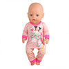 A baby doll wearing a pink unicorn pajama set with a face design and matching pants.