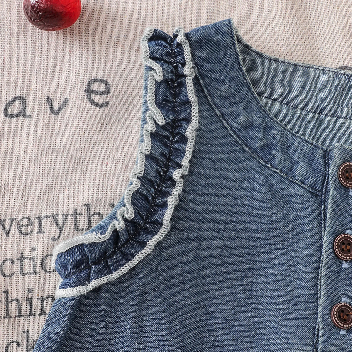 A close-up of a denim sleeveless dress for a toddler girl featuring delicate lace trim on the neckline.