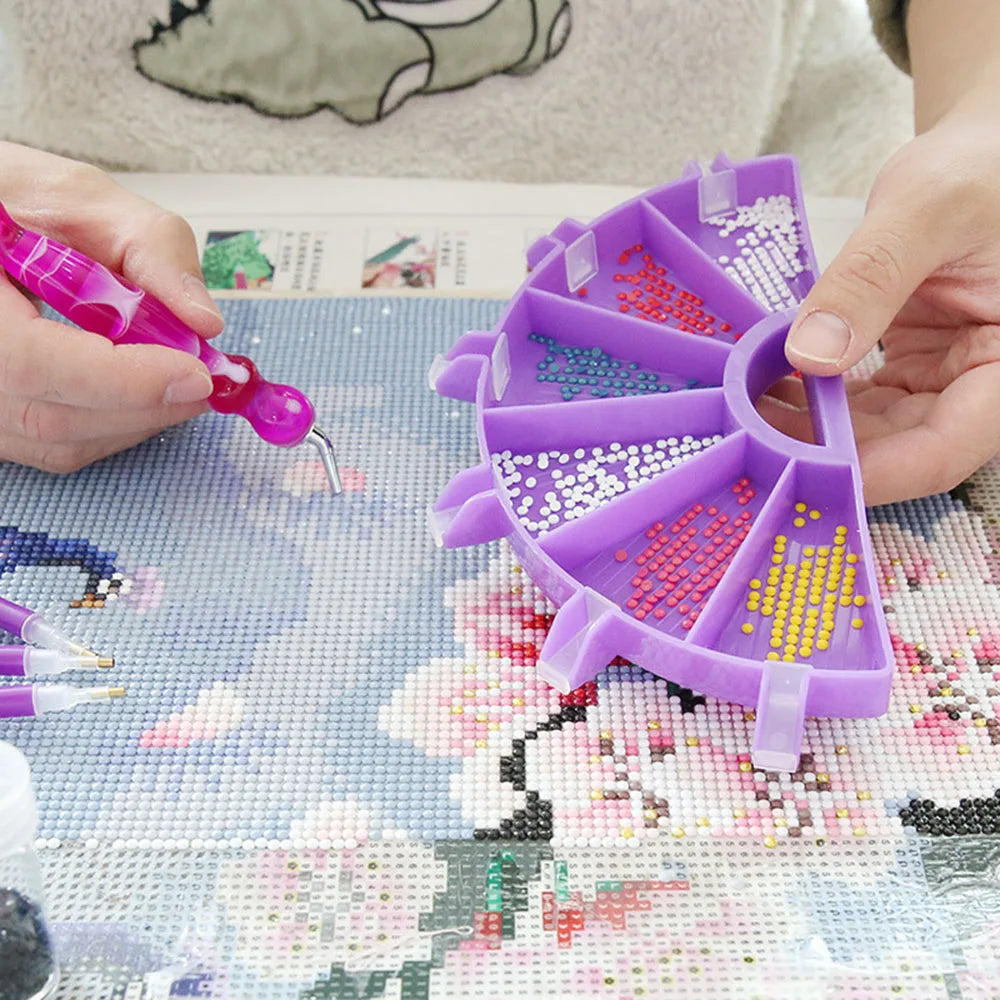 Hands are arranging colorful seed beads into a purple diamond painting organizer tray.