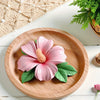 A pink hibiscus flower with a yellow center is placed on a wooden plate.