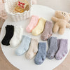 Three pairs of soft fleece socks in pastel colors including pink, yellow, beige, and gray are displayed on a white surface.