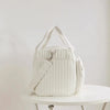A white quilted diaper bag with light beige straps resting on a white table.