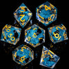 A collection of twelve blue and gold liquid core resin dice set for RPG gaming displayed on a dark surface.