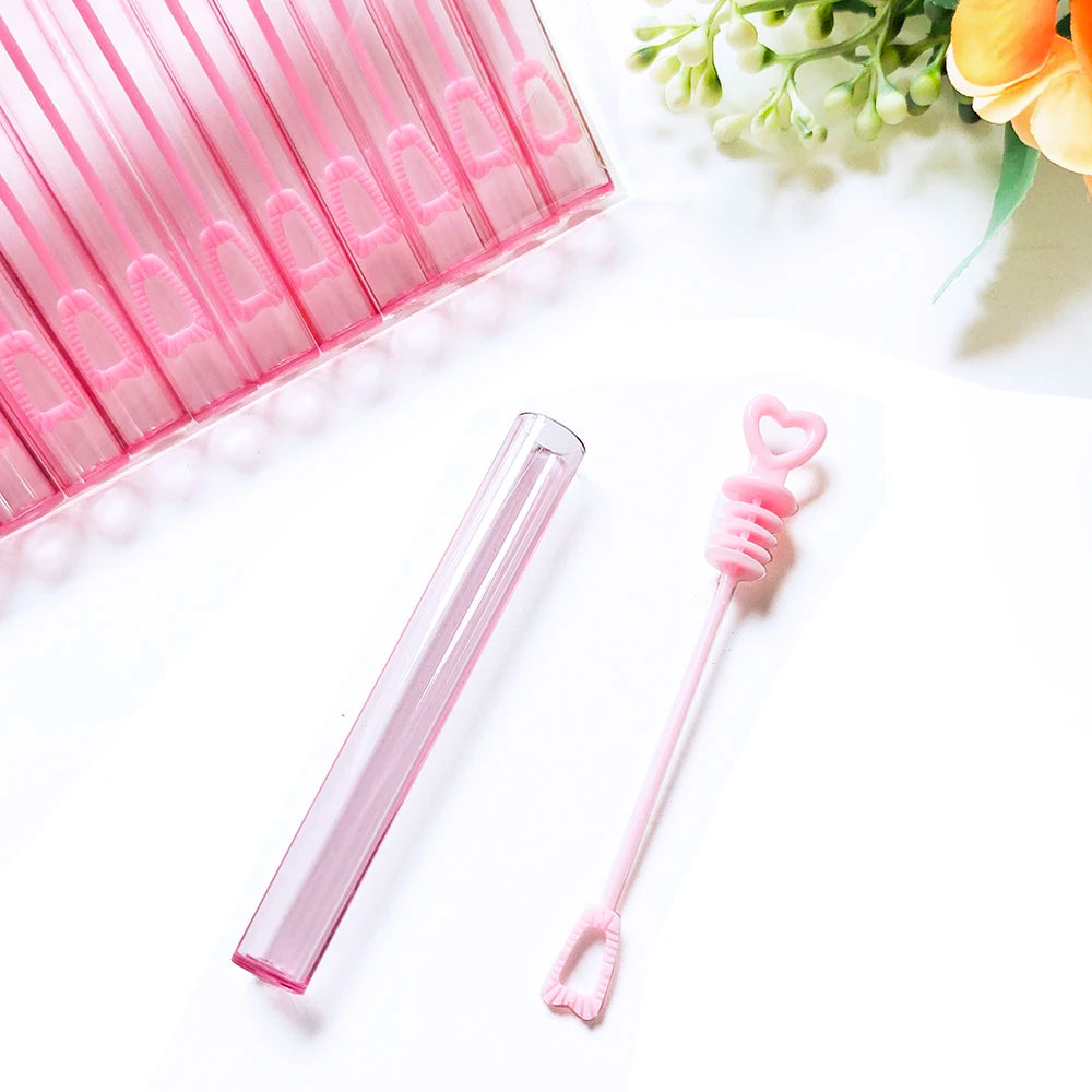 A pink glass mini bubble wand is displayed next to a pink plastic container filled with more wands.