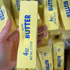 A hand holds a yellow bar of butter squishy stress relief toy packaged in clear plastic.