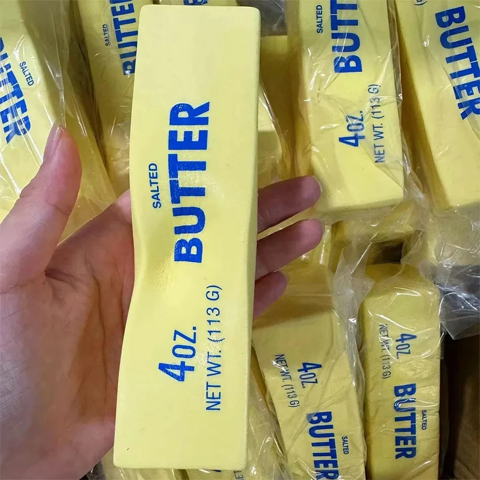 A hand holds a yellow bar of butter squishy stress relief toy packaged in clear plastic.