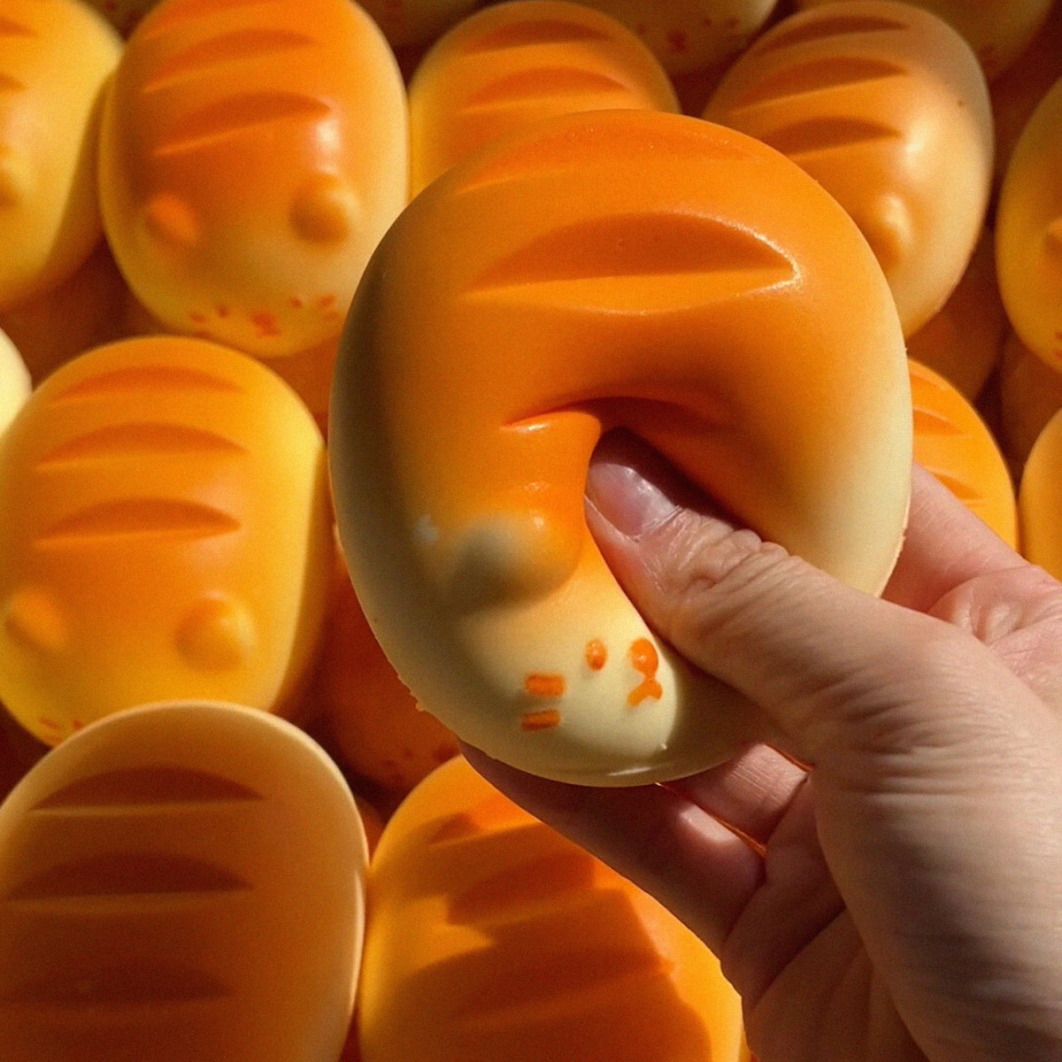 A hand holds an orange giant chick squishy toy with textured ridges against a background of similar toys.