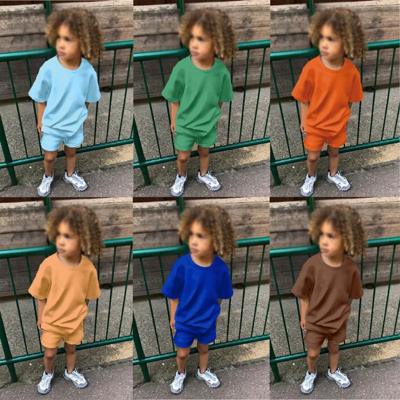 A young boy models a kids summer tracksuit set consisting of a light blue top and matching shorts.