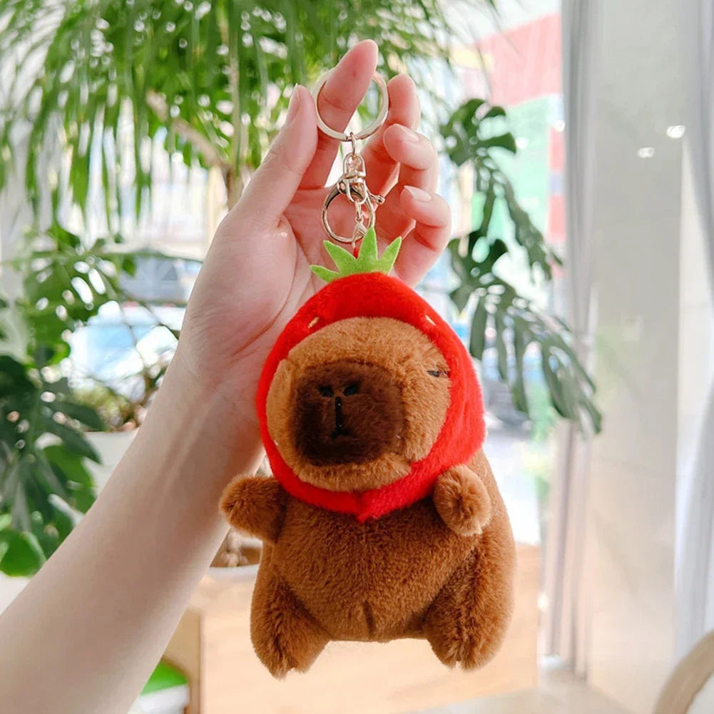 A hand holds an adorable brown capybara plush keychain charm with a green leaf detail.