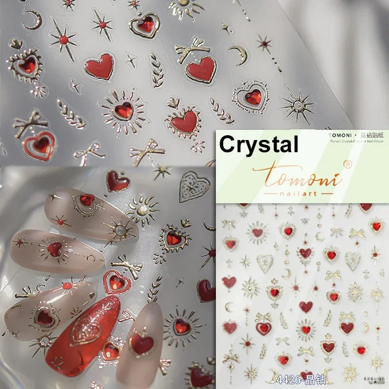 Close-up of Tomoni nail art stickers featuring red and gold heart designs, stars, and decorative elements on a clear backgrou